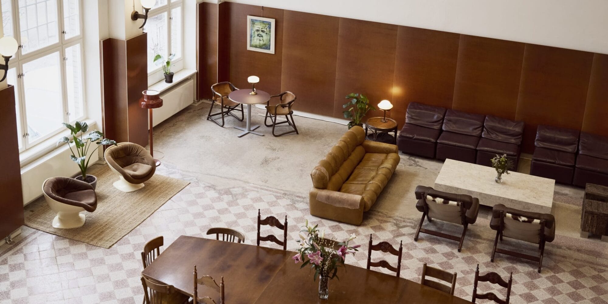 A bright room seen from above, furnished with a sofa group, long table and a couple of armchairs.